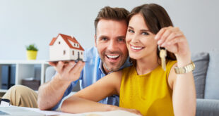 Happy couple holding keys to new home and house miniature